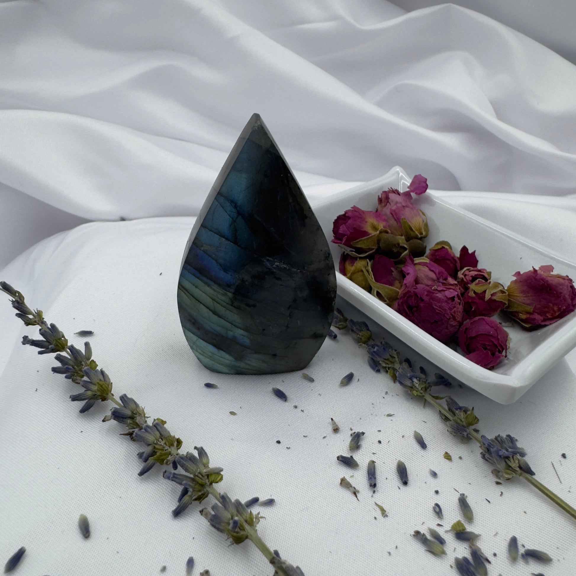 Labradorite freeform crystal standing upright on white fabric with dried roses and lavender nearby