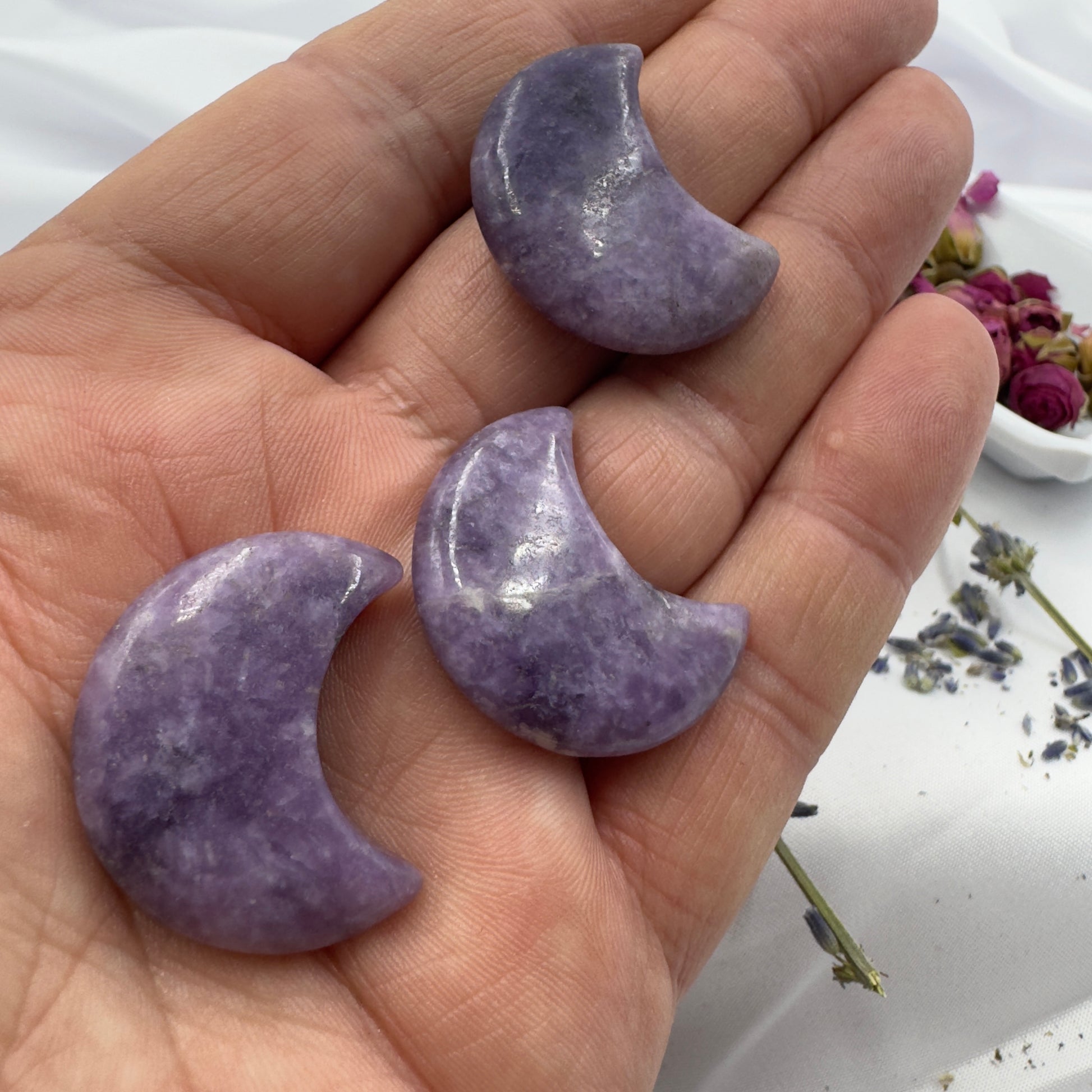 Three polished Lepidolite moon crystal crescent shapes held on a hand by Davinas