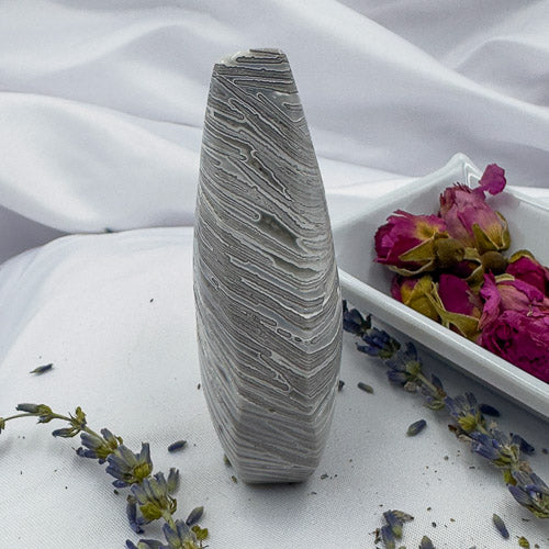 Morocco agate freeform stone standing upright on white fabric with dried flowers and pink roses nearby