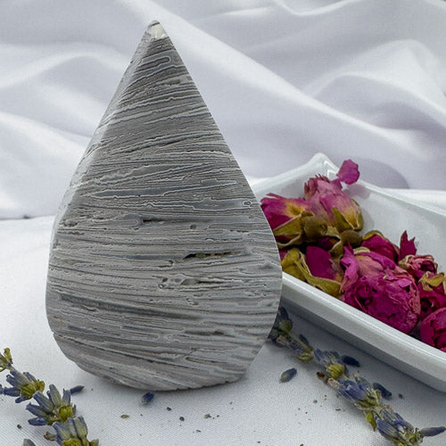 Davinas Morocco agate freeform stone with gray striped patterns displayed on white cloth with dried flowers