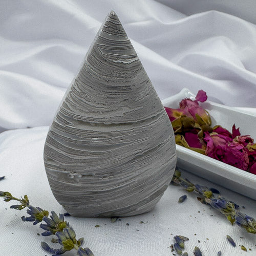 Morocco agate freeform stone with gray layered patterns displayed on white cloth with dried flowers