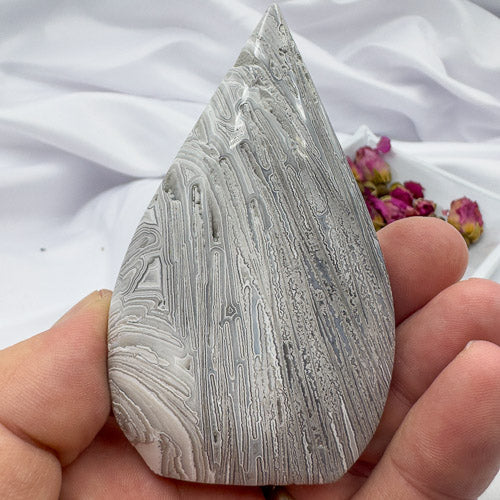 Hand holding a polished Morocco agate stone with gray and white layered patterns