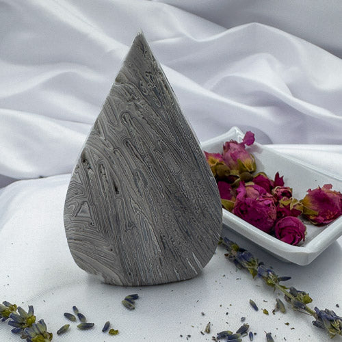 Polished Morocco agate stone with intricate gray patterns displayed on white fabric with dried flowers