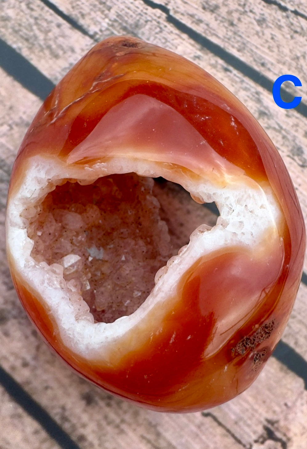 Davinas Carnelian geode druzy with vibrant orange and white crystal interior on wooden surface