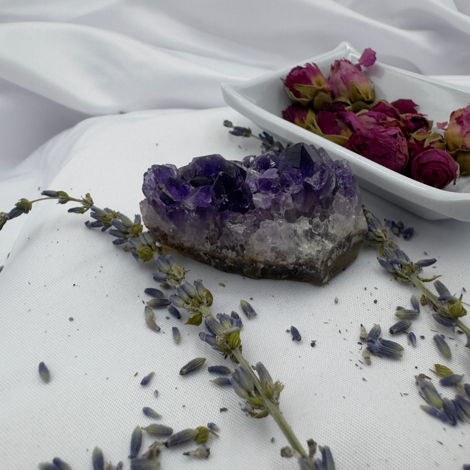 Davinas raw amethyst crystal cluster displayed with dried lavender and rose buds on white fabric