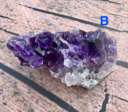 Davinas raw amethyst crystal cluster with deep purple and white crystals on a wooden surface