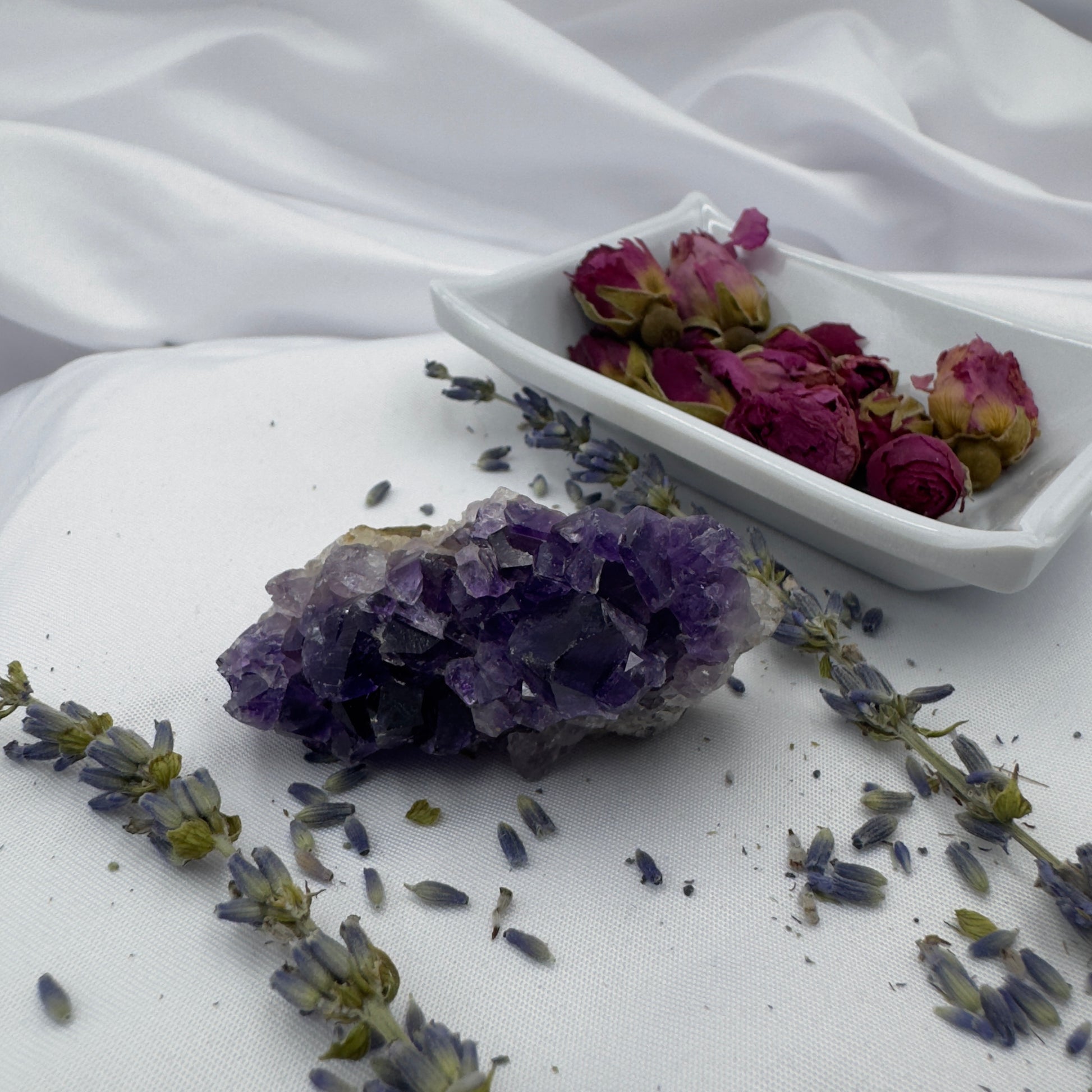 Davinas raw amethyst crystal cluster surrounded by dried lavender and rosebuds on white fabric