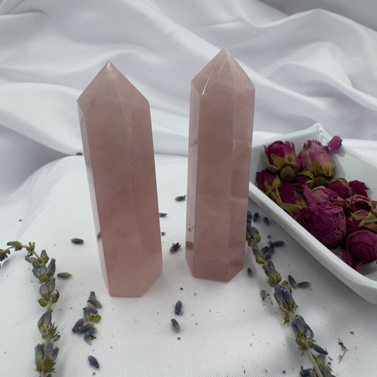 Two polished rose quartz tower point crystals standing on white fabric with dried flowers nearby