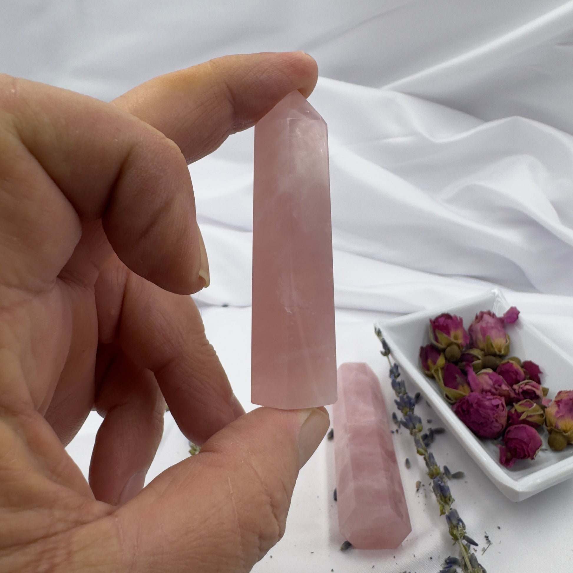 Hand holding a polished rose quartz tower point with dried flowers on a white fabric background