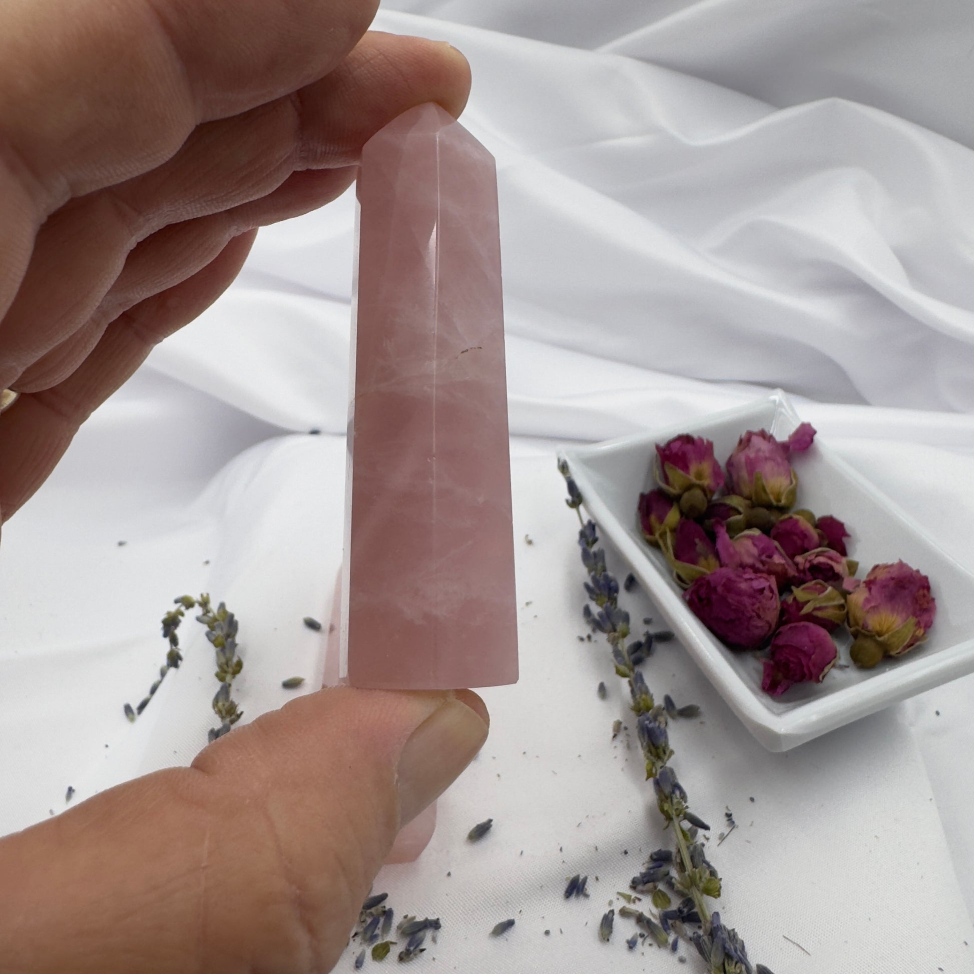 Hand holding a pink rose quartz tower point crystal with dried flowers in the background