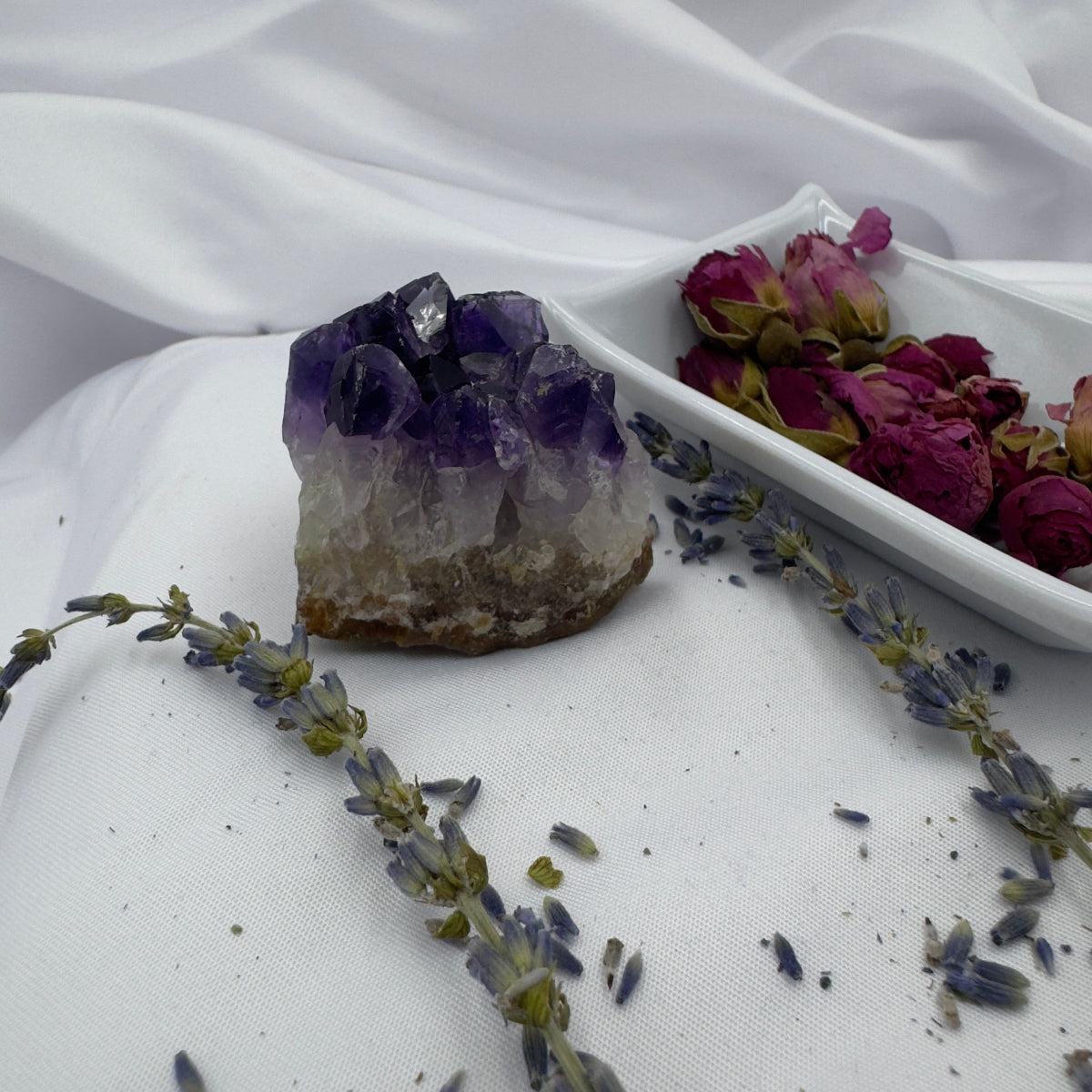 Davinas amethyst raw crystal cluster displayed with dried rose buds and lavender on white fabric