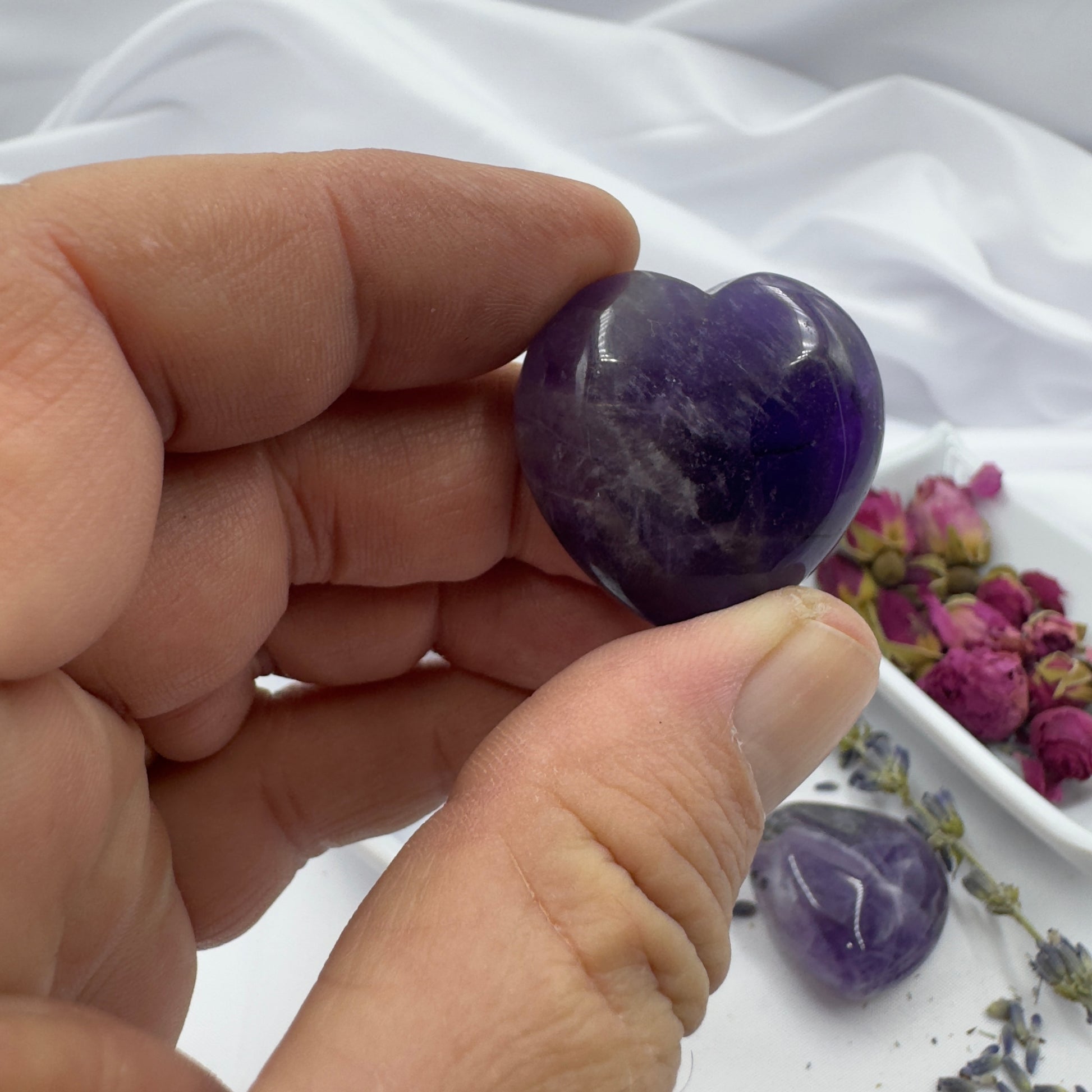 Hand holding polished chevron amethyst heart crystals with dried flowers in the background