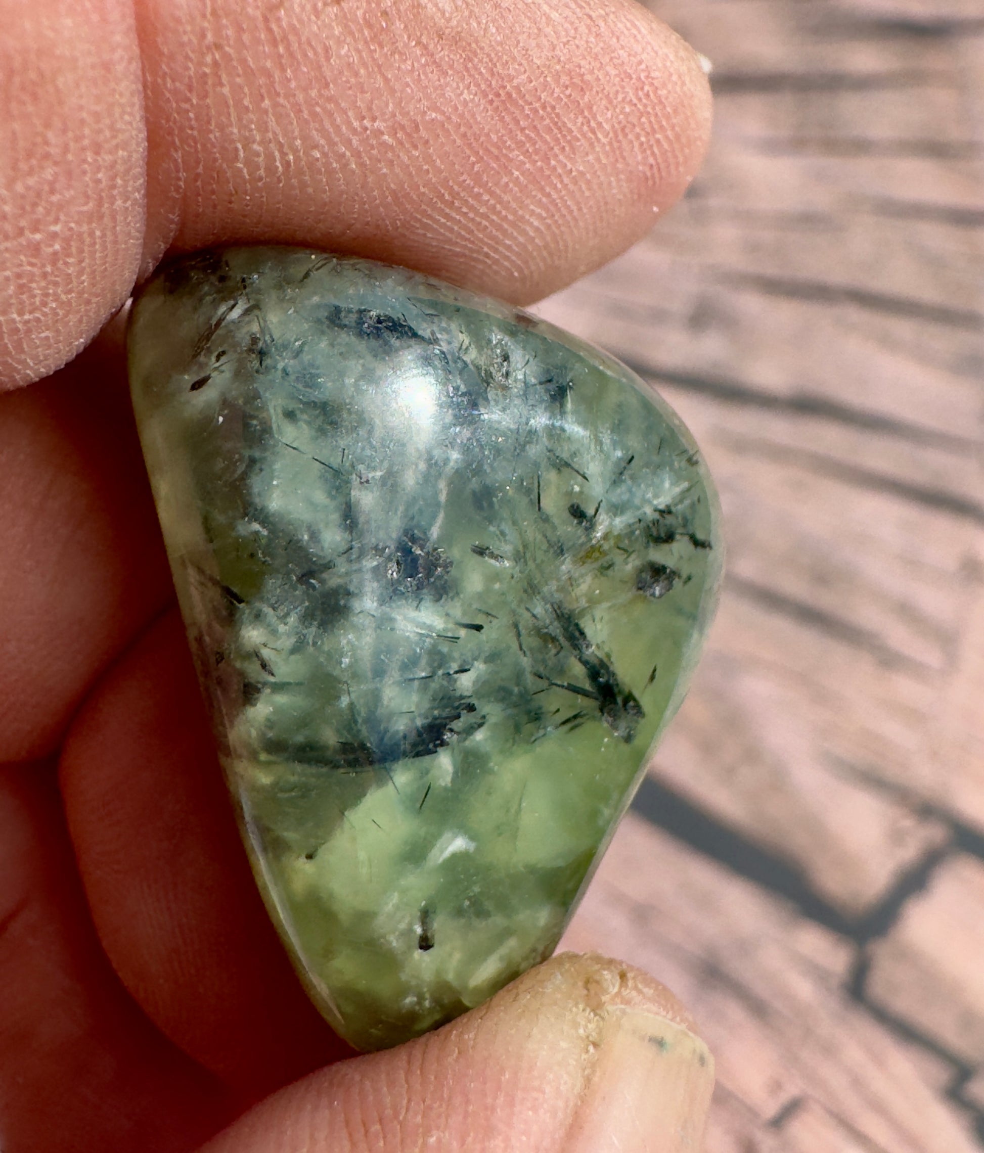 Close-up of a hand holding a green prehnite tumbled stone with polished surface and natural inclusions