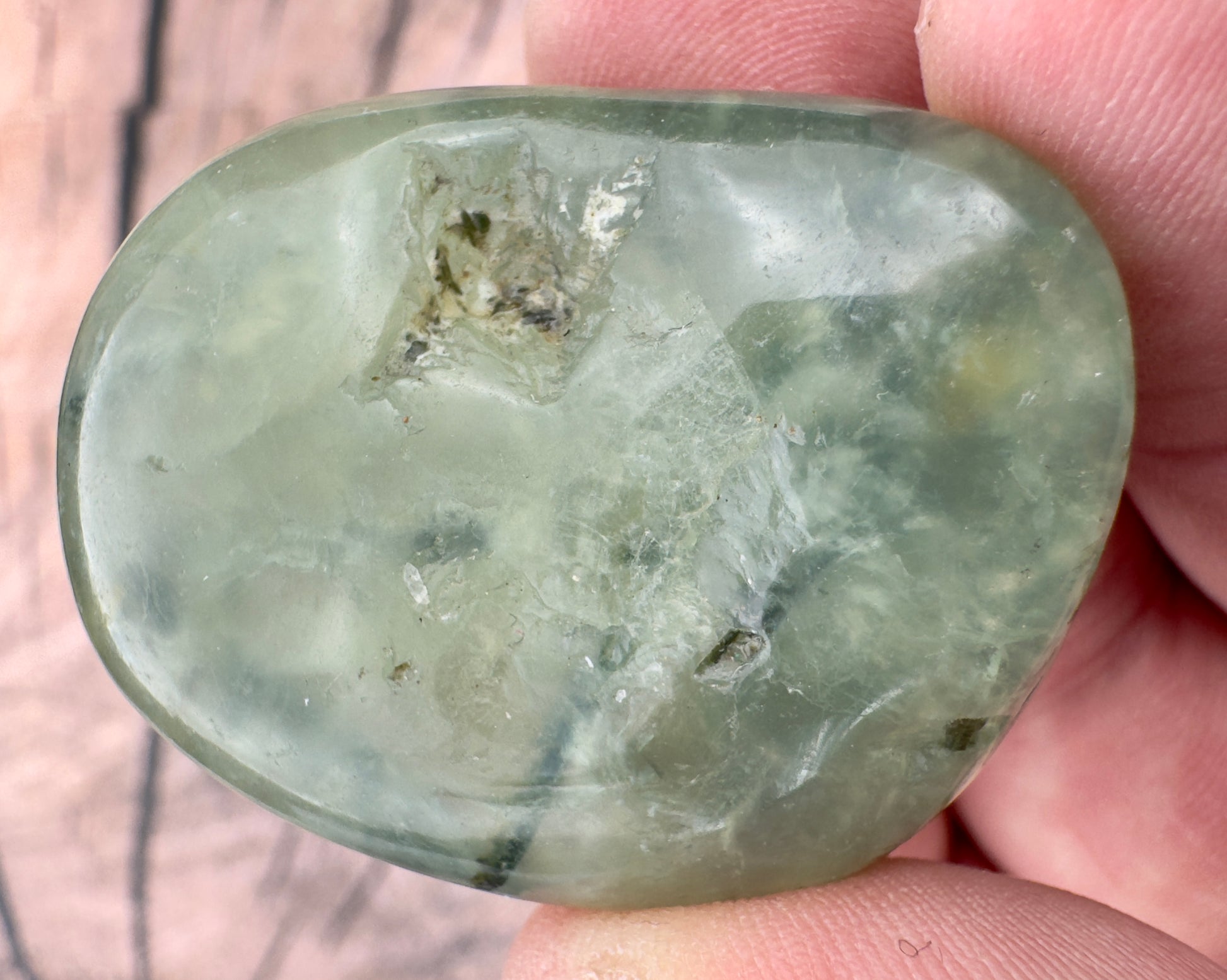 Close-up of a green prehnite tumbled stone held between fingers showing smooth polished surface