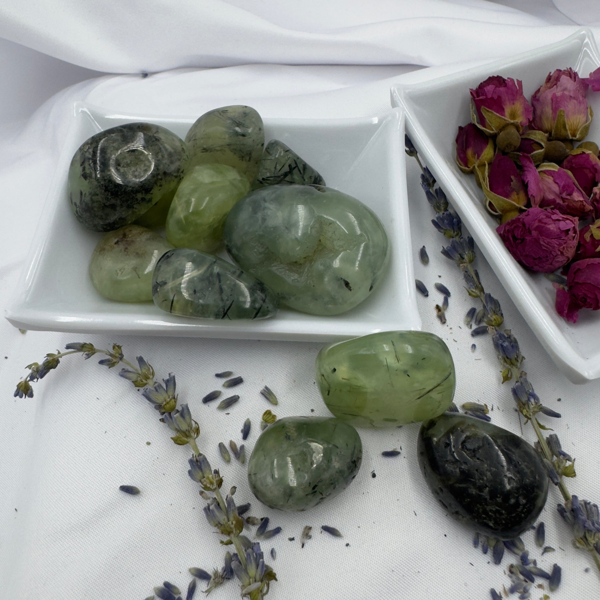 Davinas green prehnite tumbled stone collection displayed on white ceramic dishes with dried flowers