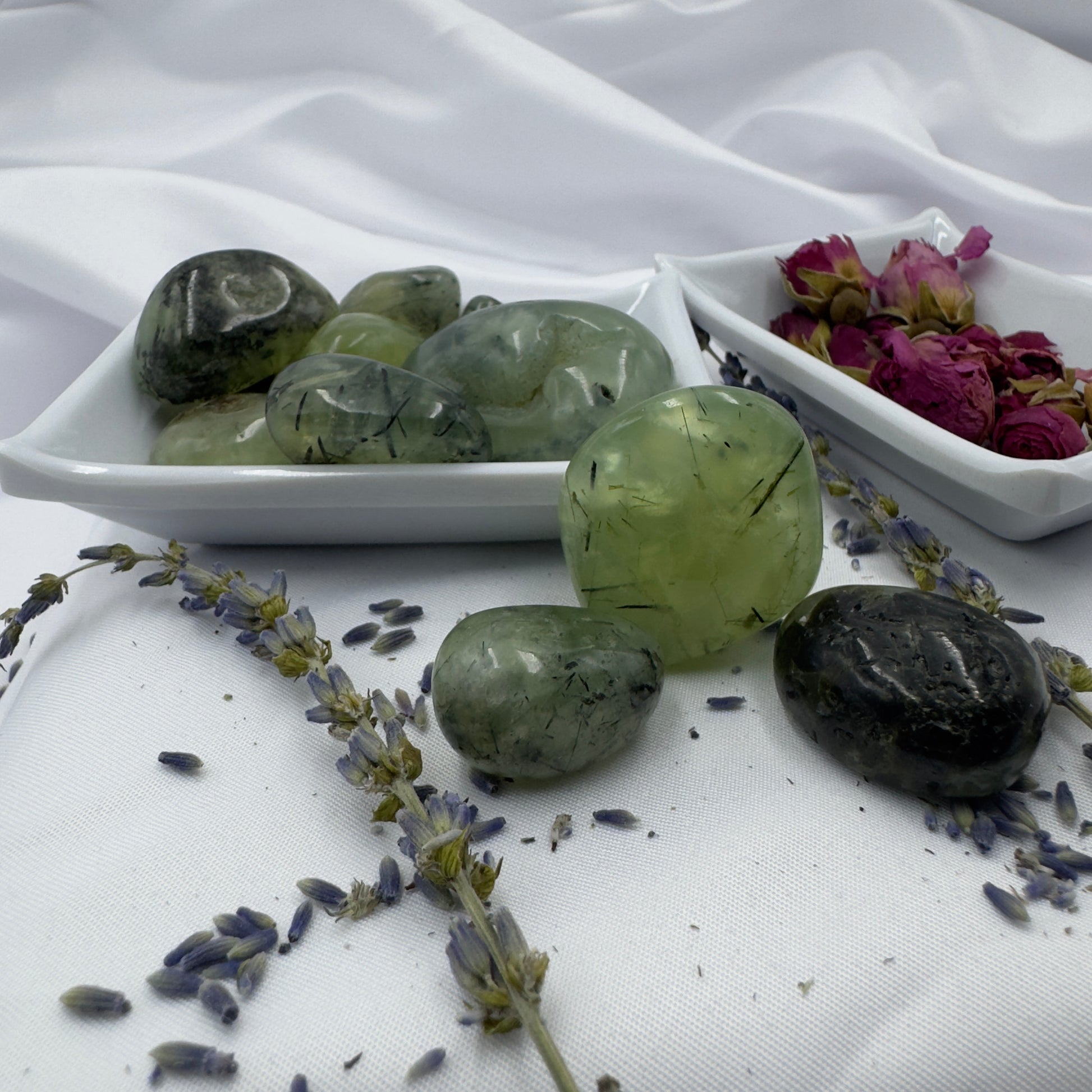 Davinas green prehnite tumbled stone collection displayed with dried lavender and rose petals on white fabric