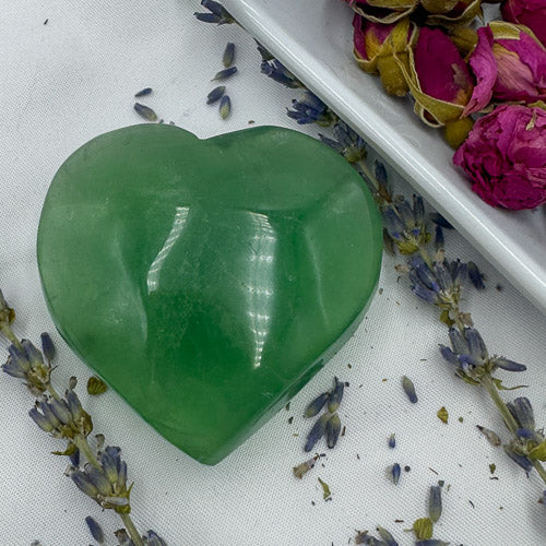Heart-shaped green fluorite stone surrounded by dried flowers from the premium fluorite stone collection