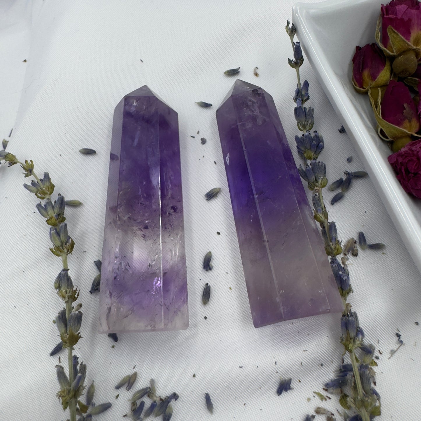 Davinas Amethyst Tower Point crystals surrounded by dried lavender and rose buds on white surface