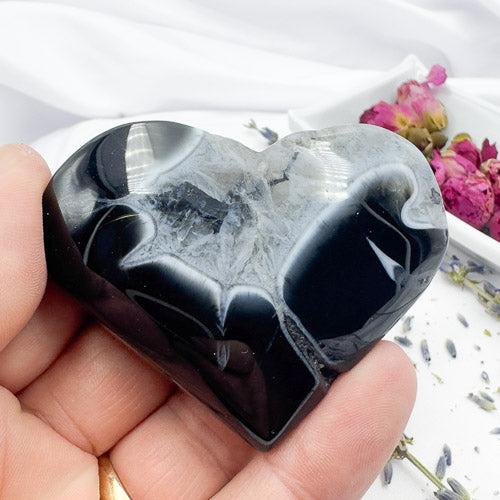 Hand holding a heart-shaped polished black stripe agate stone with smooth texture and natural patterns