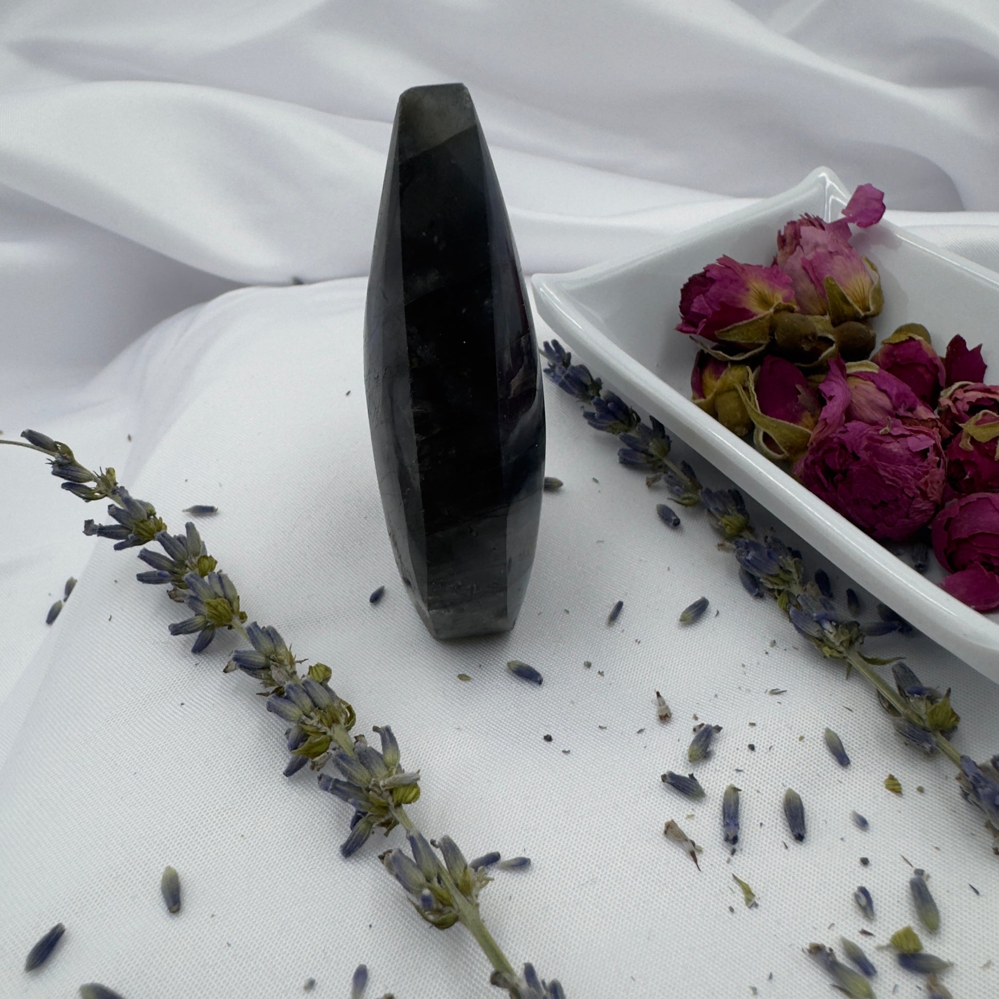 Labradorite freeform crystal standing upright on white fabric with dried purple flowers and a white dish