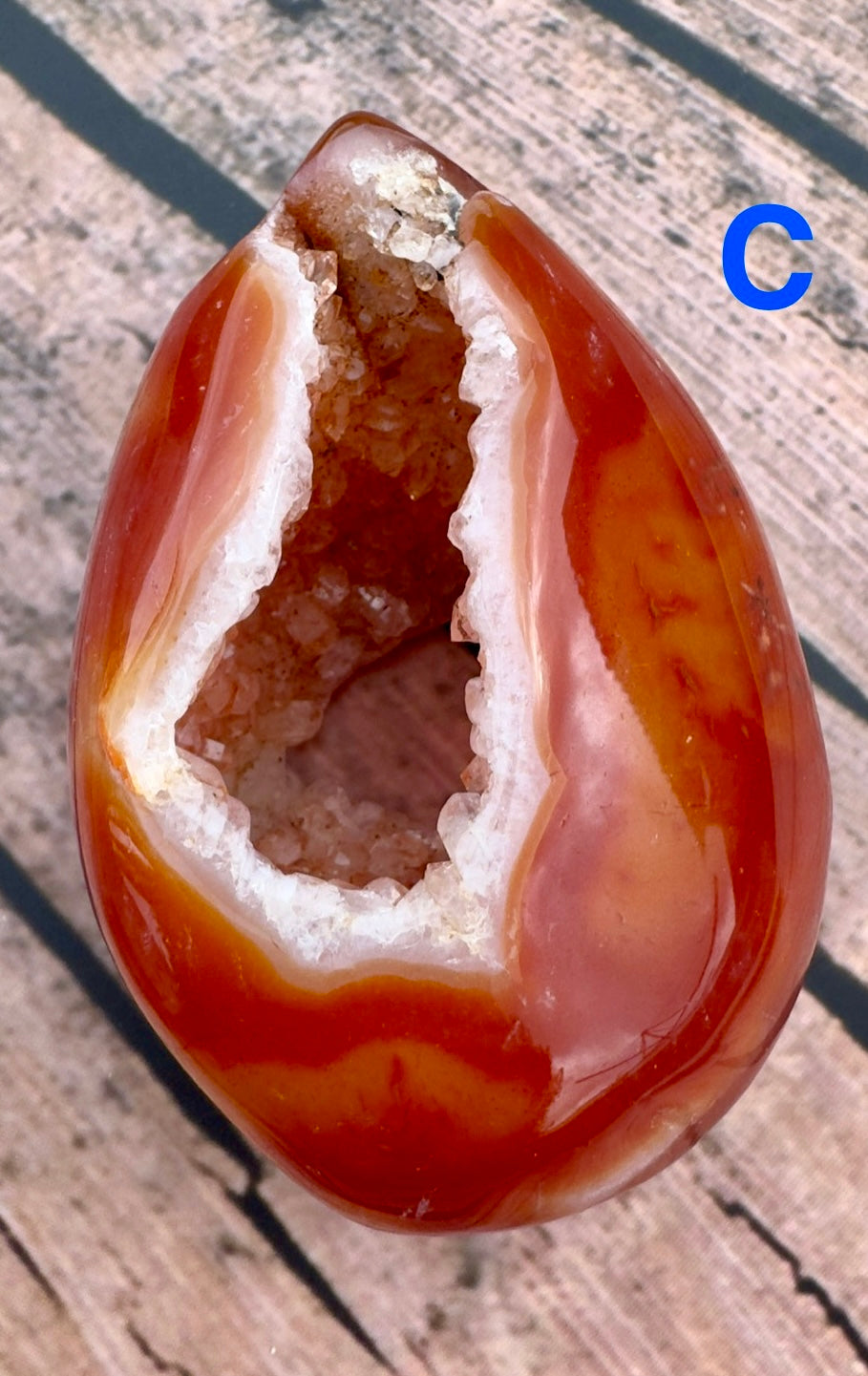 Davinas carnelian geode druzy with vibrant orange outer layer and sparkling crystal interior on wooden surface